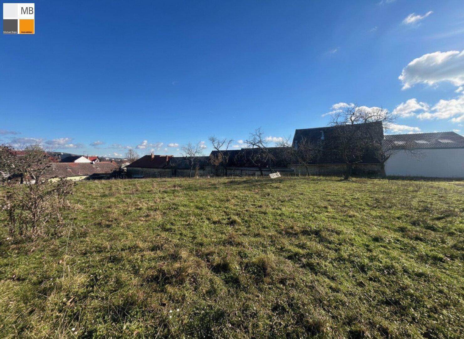 Großes Grundstück mit Wiese und Bäumen, umgeben von ländlicher Bebauung unter blauem Himmel.