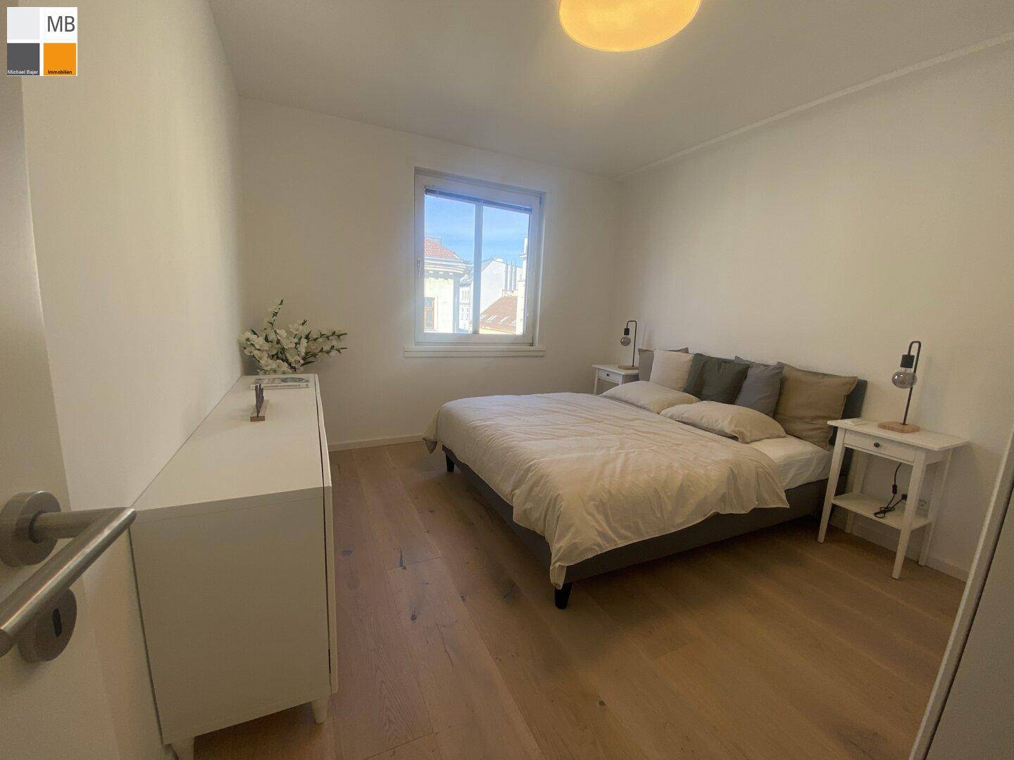 Helles Schlafzimmer mit Holzboden und einem Fenster, das viel Tageslicht hereinlässt.
