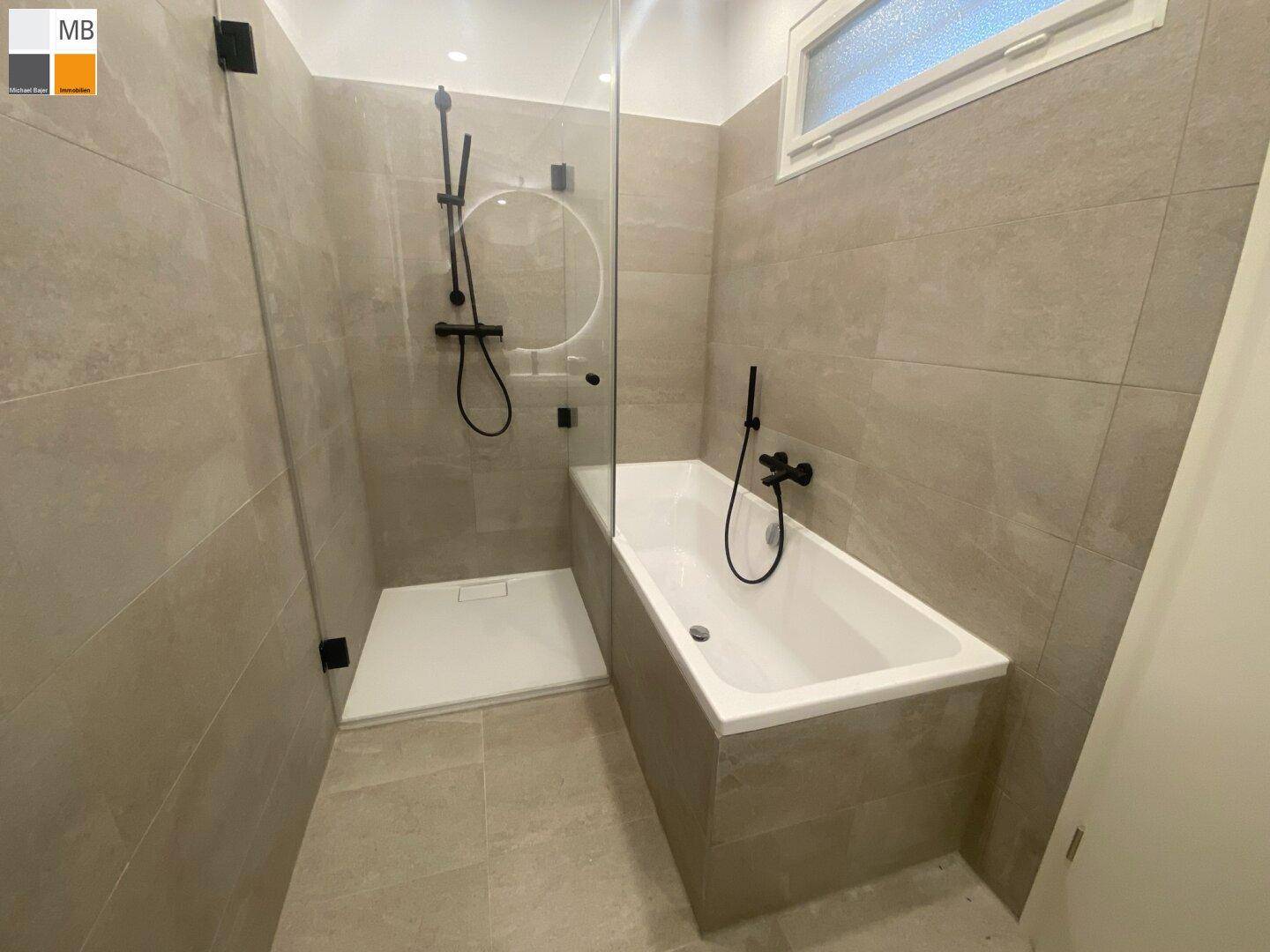 Modernes Badezimmer mit Badewanne, Duschbereich und hellgrauen Fliesen.
