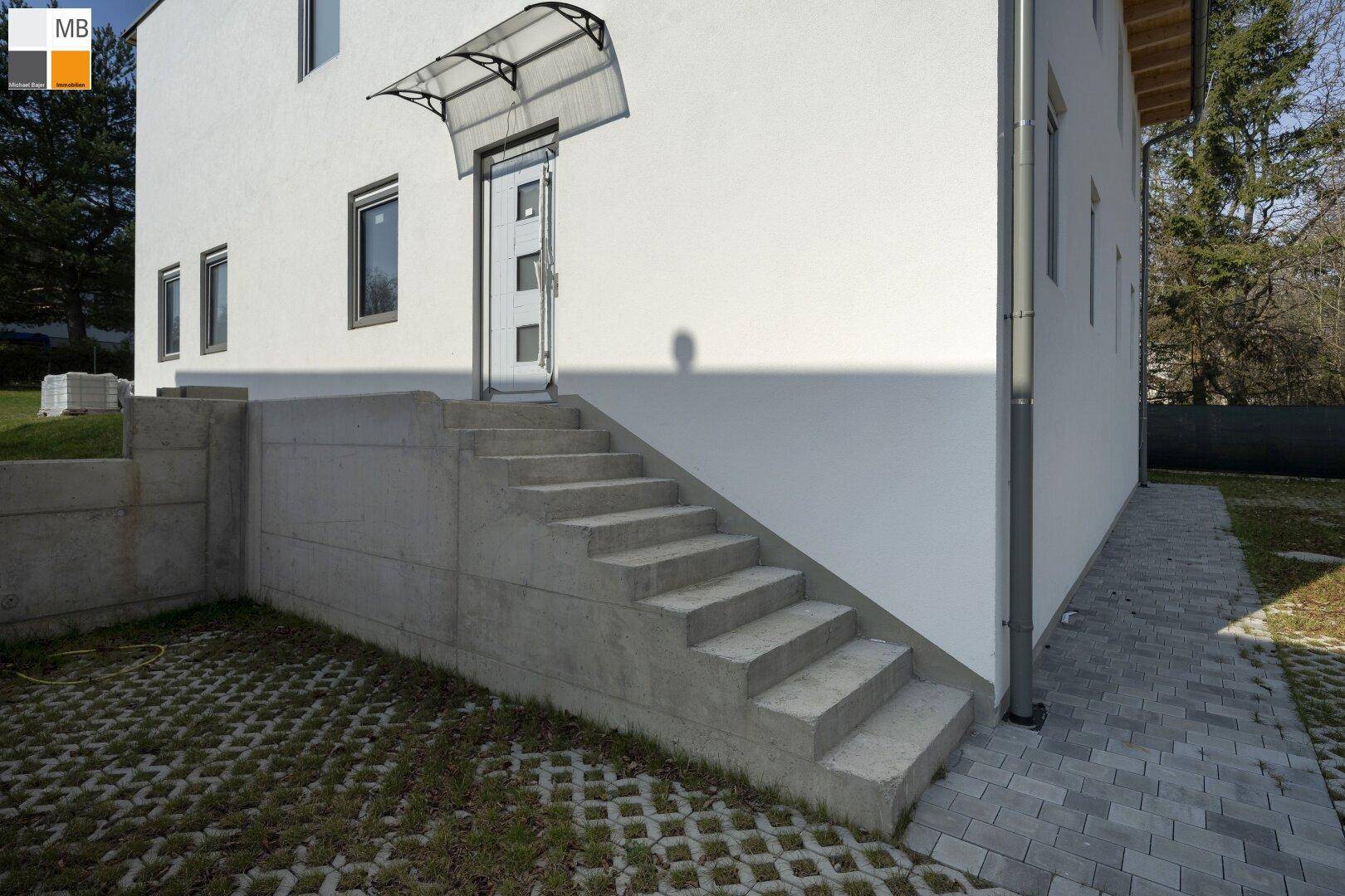 Seitlicher Eingangsbereich des Hauses mit Betontreppe und gepflastertem Vorplatz.