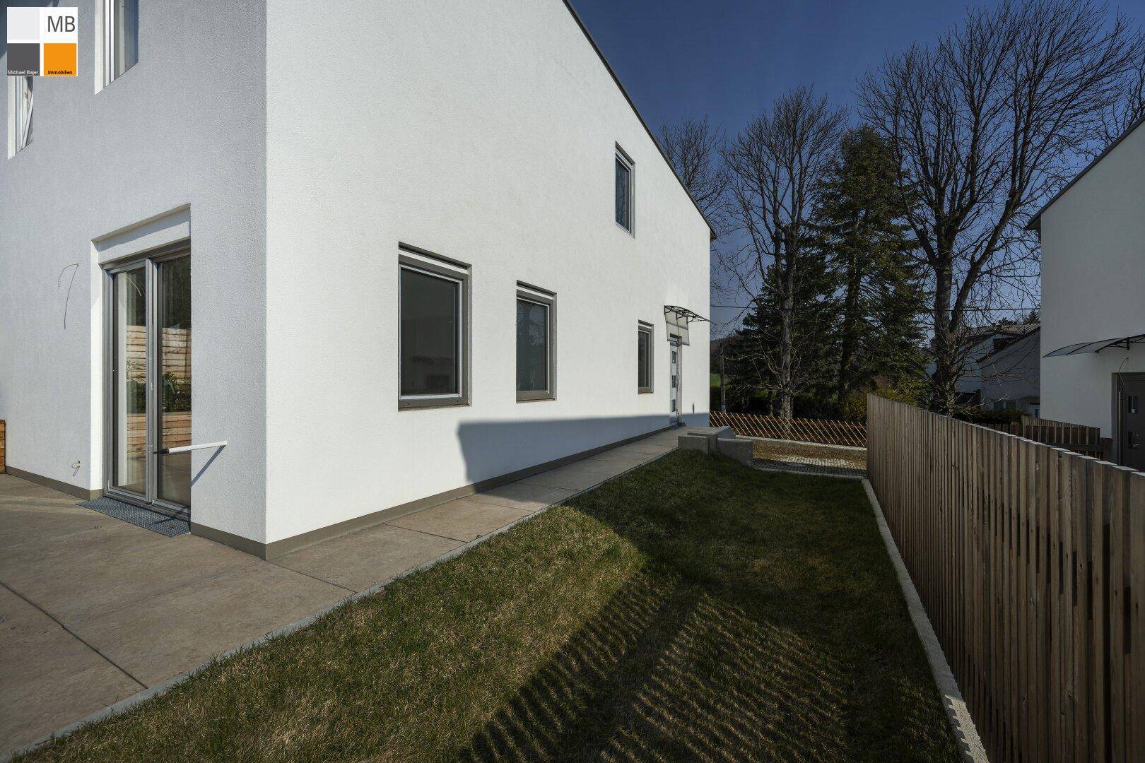 Seitenansicht des Hauses mit einem schmalen Gartenstreifen und einem gepflasterten Weg.