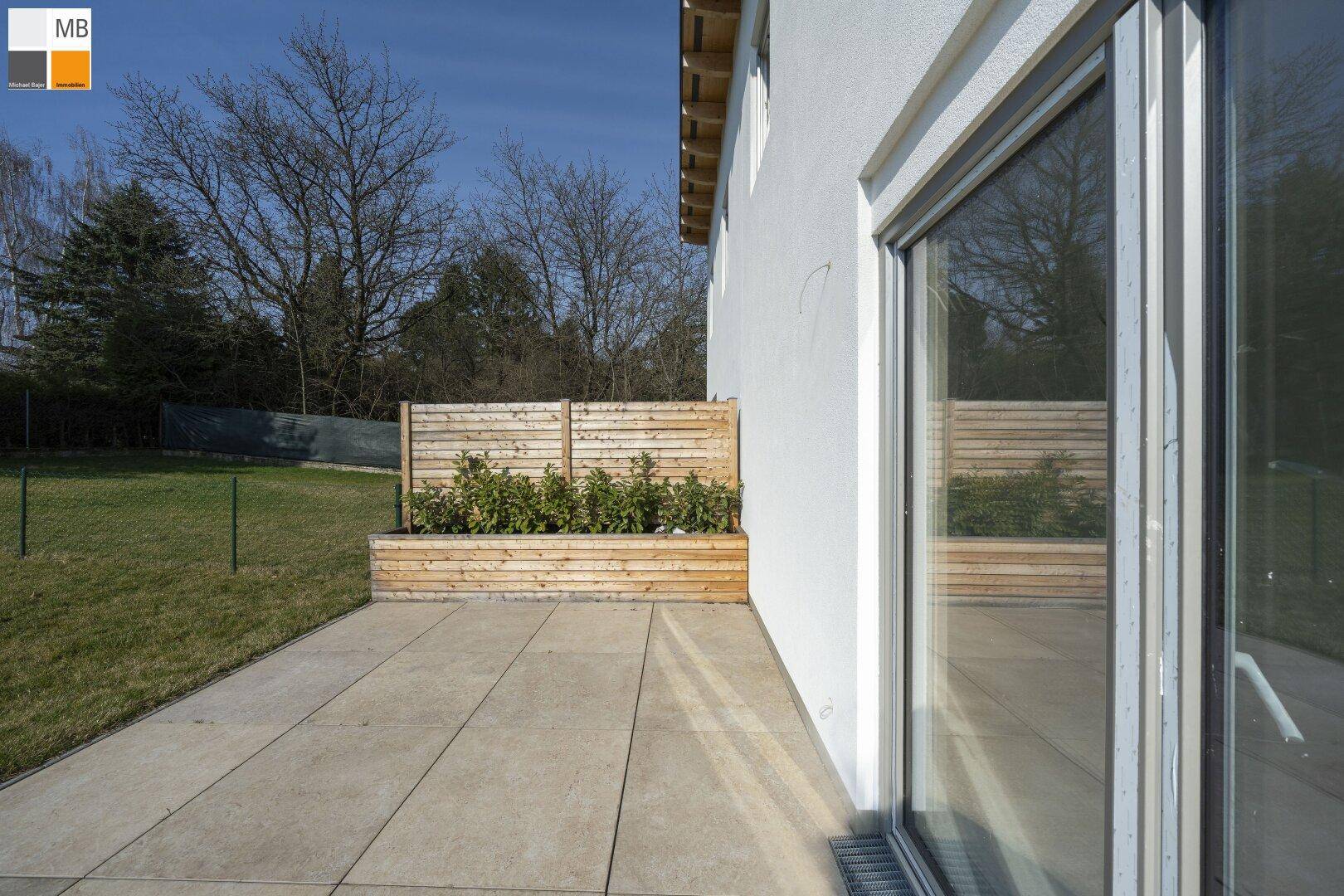 Seitliche Terrasse mit Schiebetür zum Haus und Blick auf den angrenzenden Garten.
