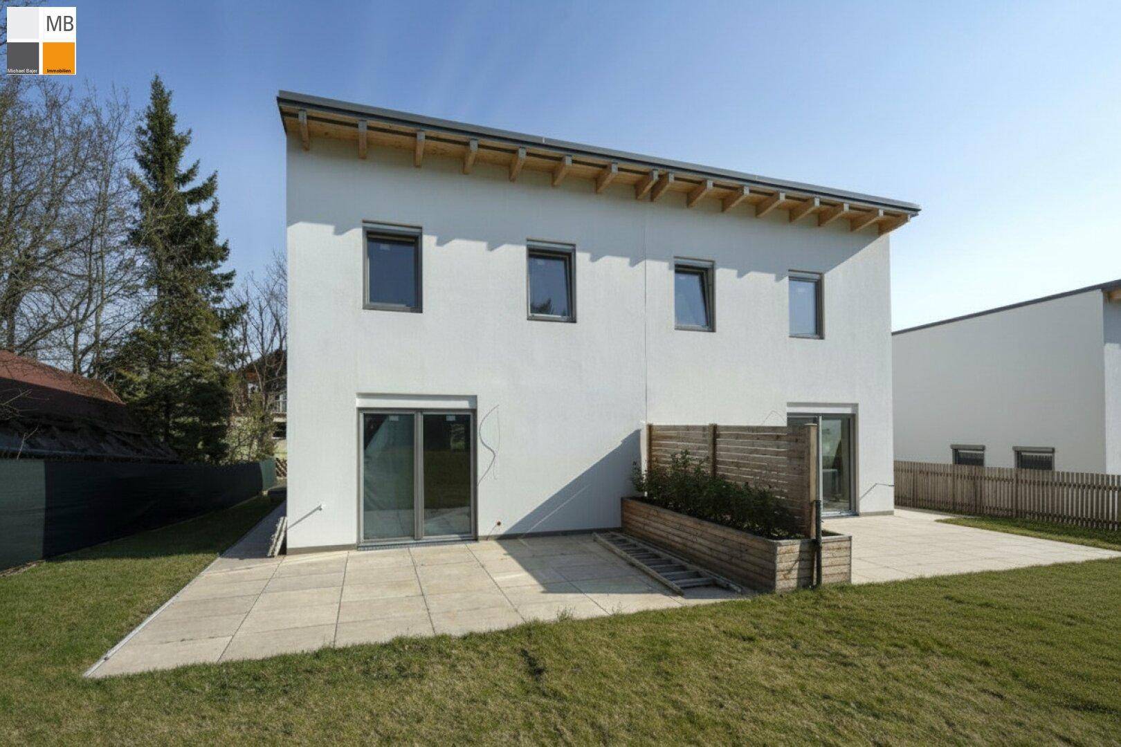Rückansicht des modernen Hauses mit großer Terrasse und angrenzendem Gartenbereich.