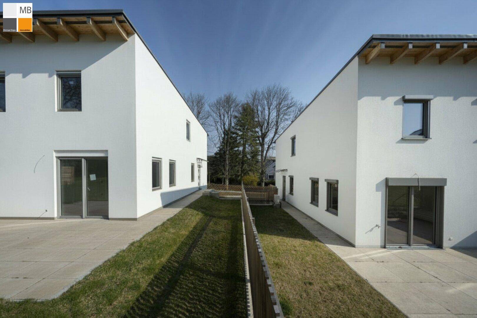 Blick zwischen zwei modernen Häusern auf einen gemeinsamen Gartenbereich mit Rasenfläche.