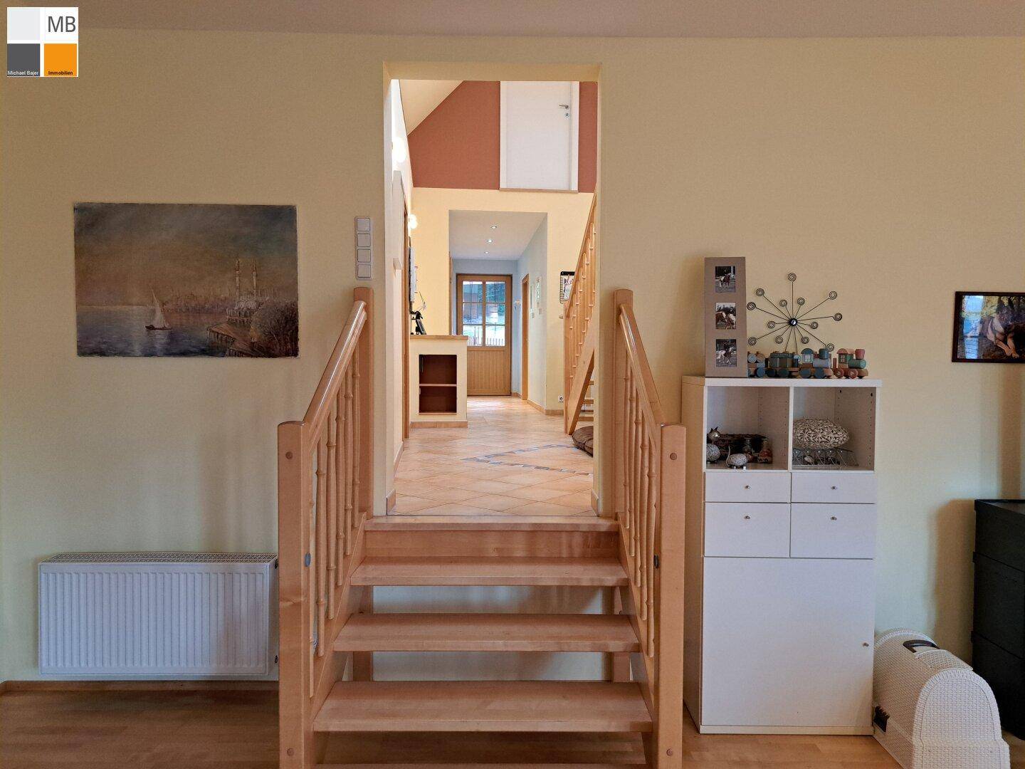 Heller Flur mit Holztreppe, Holzboden und Blick in den Eingangsbereich.