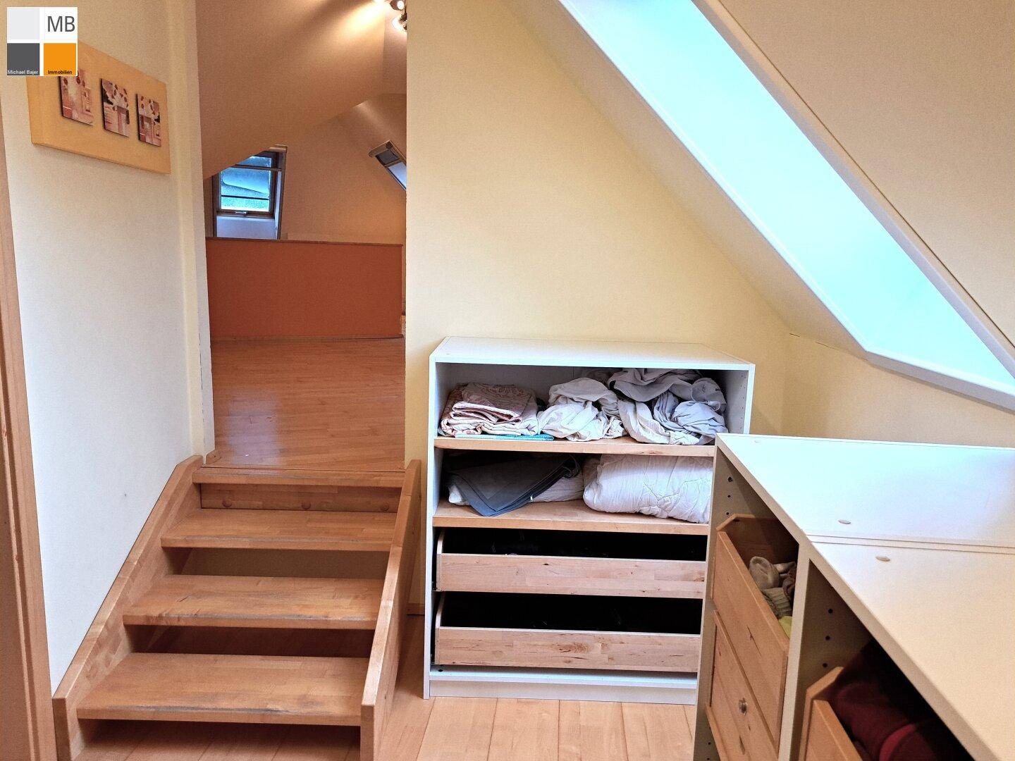 Holztreppe führt zu einem offenen Dachbodenbereich mit Stauraum und Dachfenster.