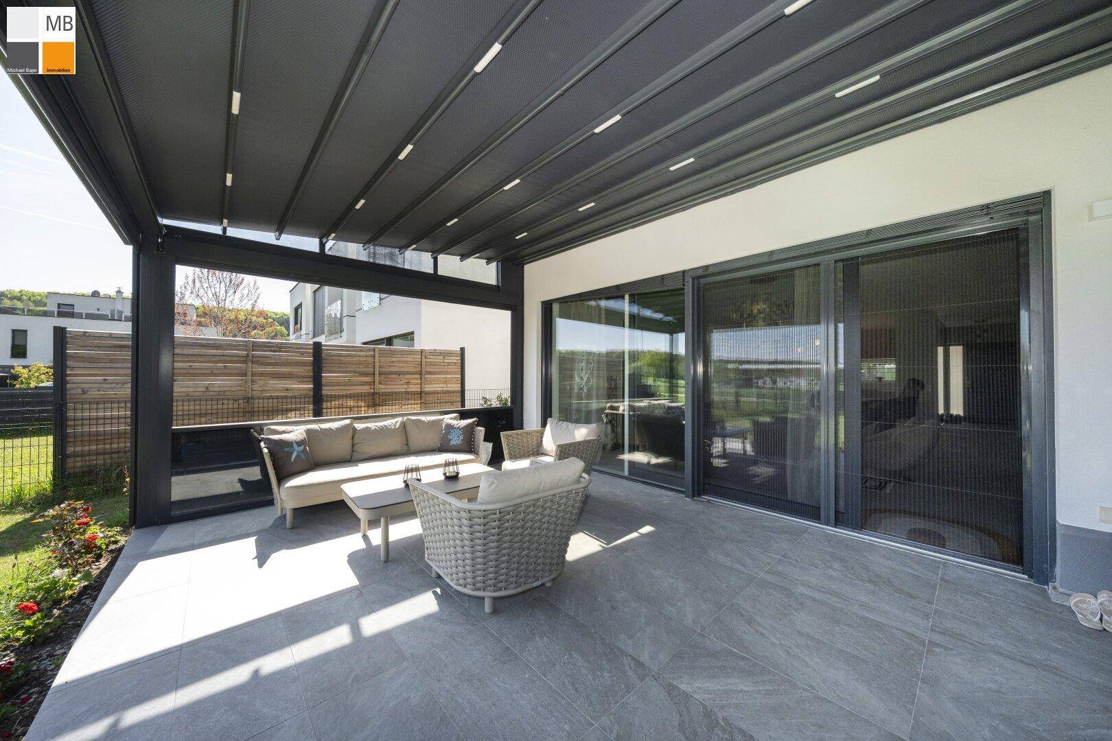 Moderne überdachte Terrasse mit bequemen Loungemöbeln und Blick ins Grüne, ideal zum Entspannen.