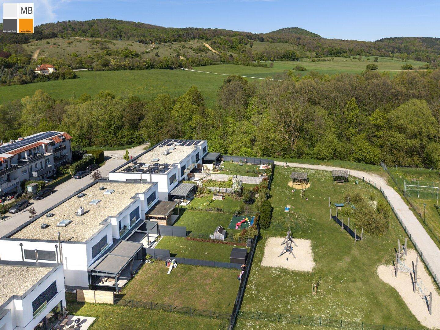 Weitläufige Luftaufnahme einer Wohnsiedlung mit angrenzenden Grünflächen und Hügellandschaft.