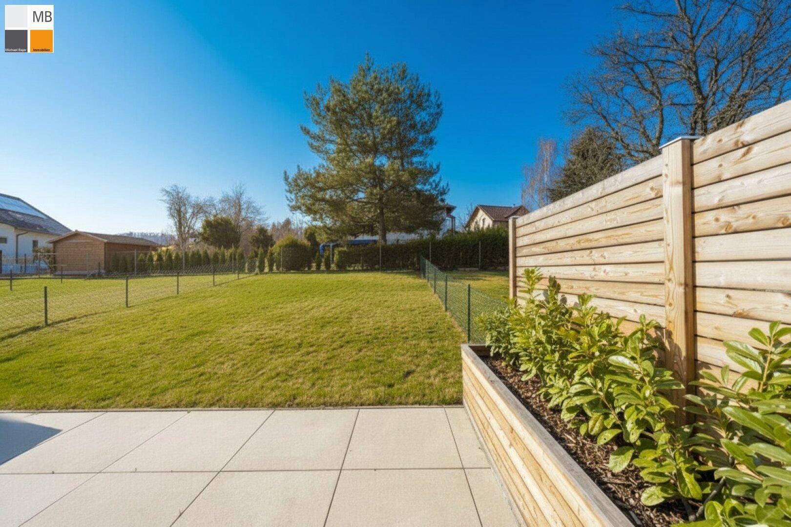 Gepflegter Garten mit Rasenfläche und einer modernen Terrasse, umgeben von einem Holzzaun.