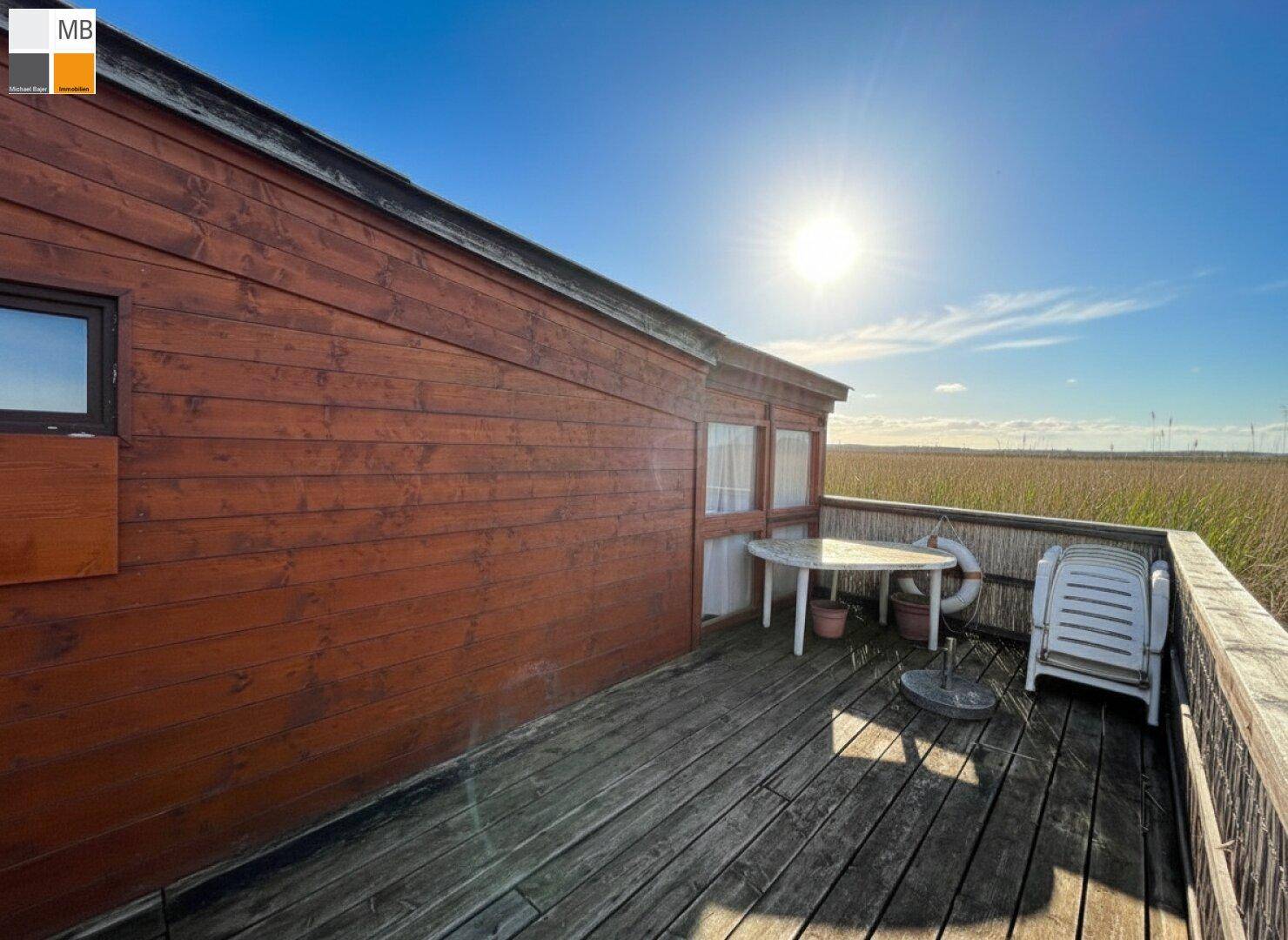 Sonniger Terrassenbereich am Holzhaus mit einfacher Bestuhlung und weitem Blick.