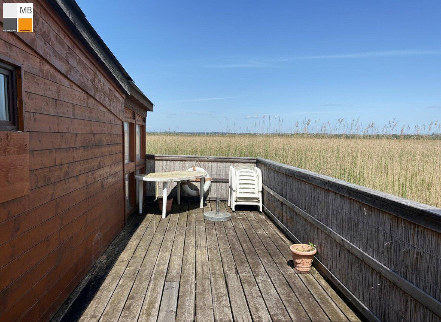 Sonniger Terrassenbereich am Holzhaus mit einfacher Bestuhlung und weitem Blick.