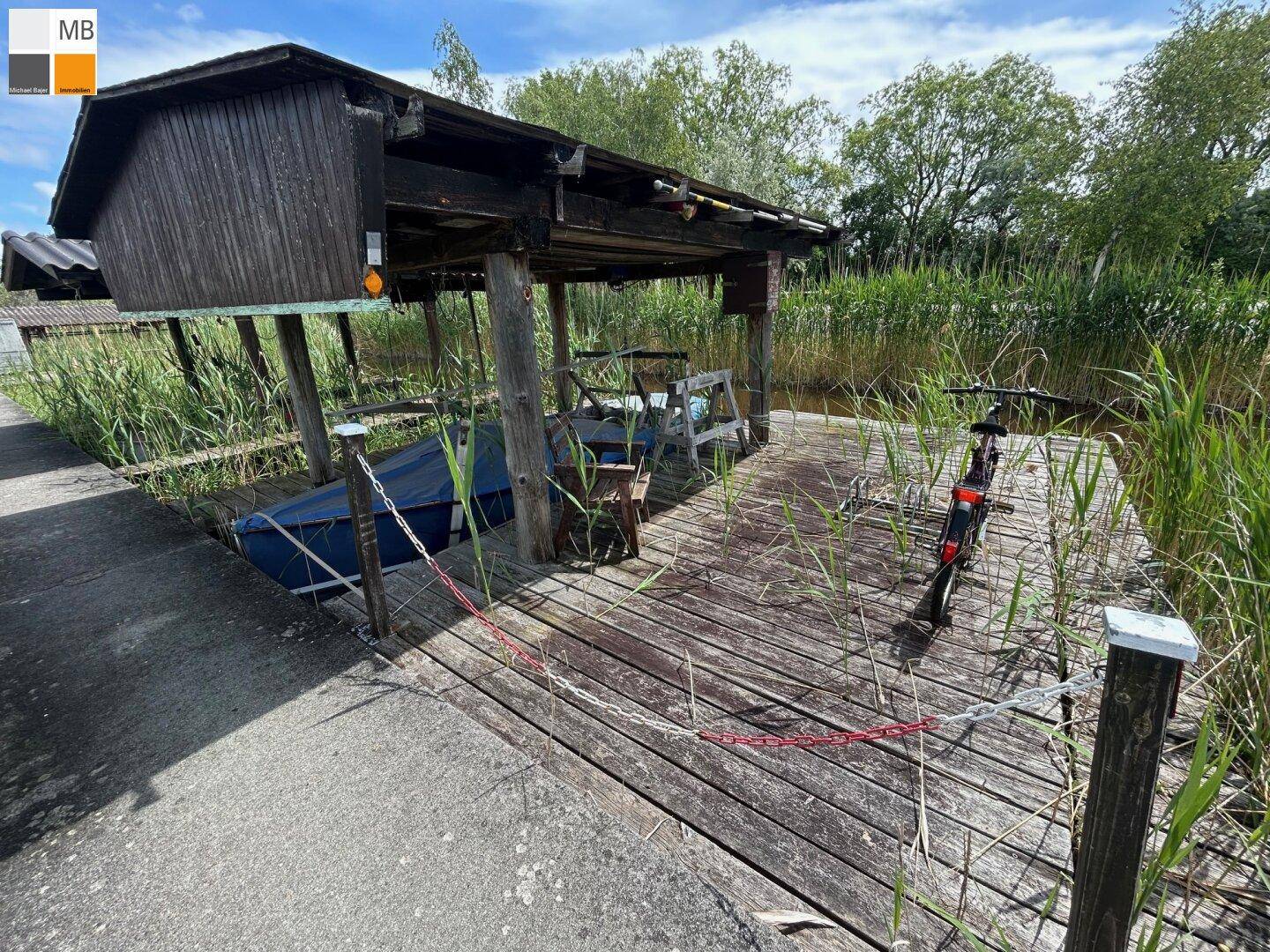 Rustikales Bootshaus mit überdachtem Liegeplatz und Holzsteg am Wasser.