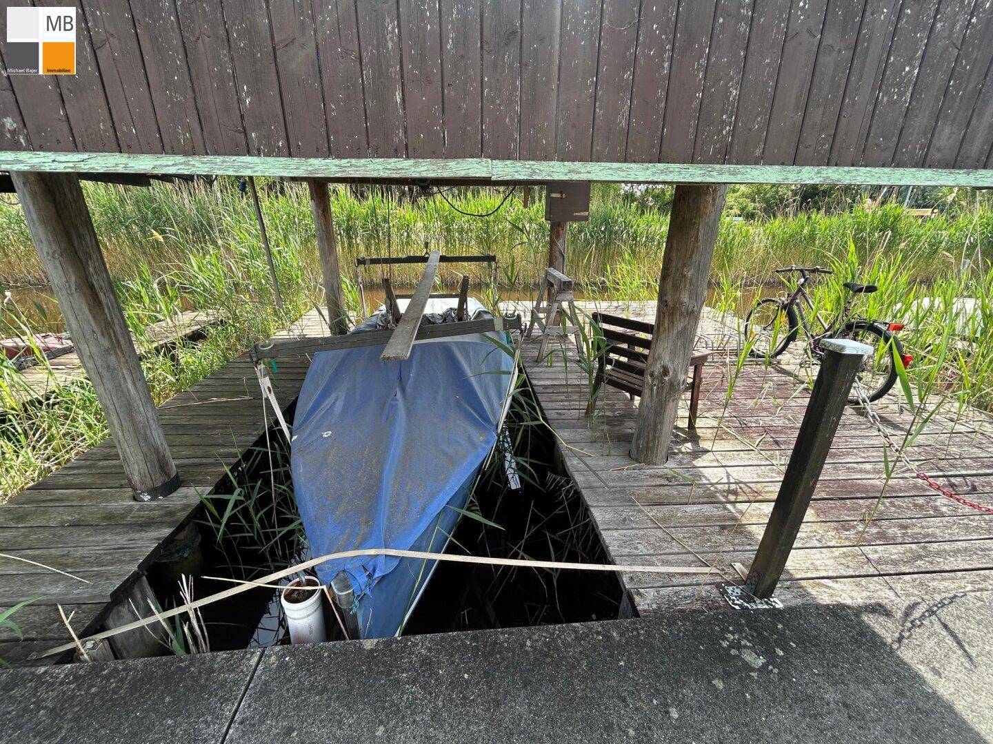 Überdachter Bootsliegeplatz mit einem abgedeckten Boot und Holzsteg.