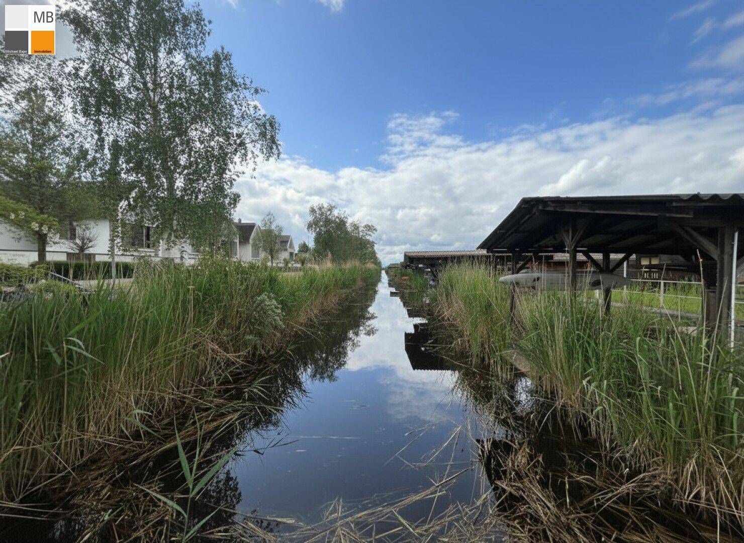 Schmaler Wasserweg mit Bootshäusern und Häusern entlang der Ufer unter blauem Himmel.