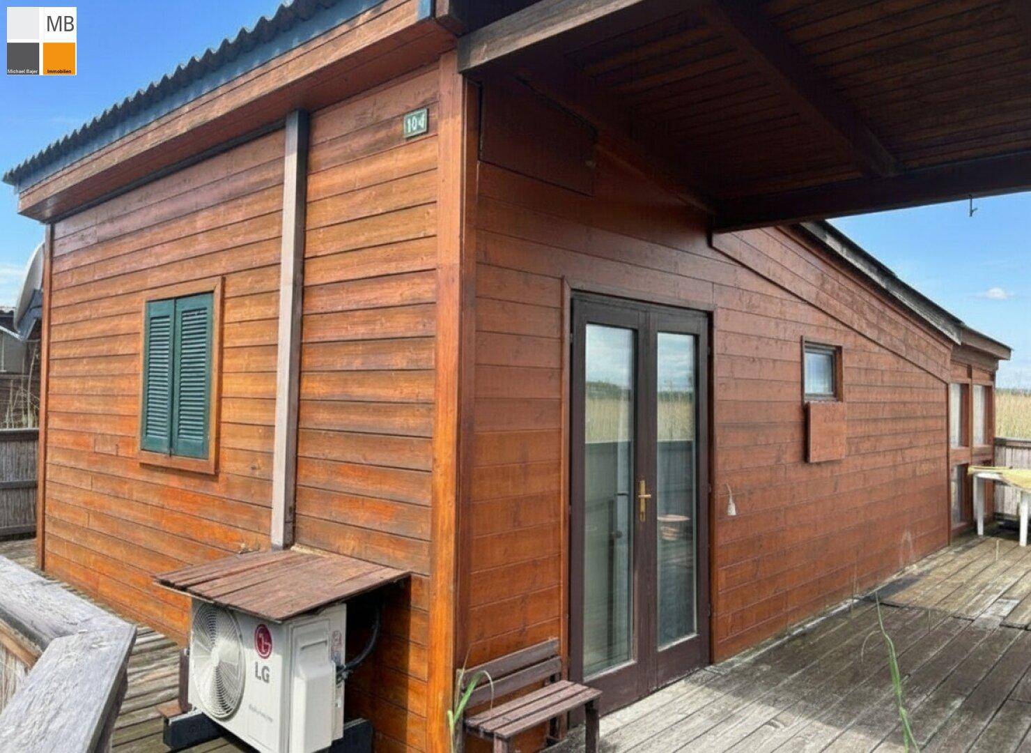 Seitenansicht des Holzhauses mit Terrassentür und Außenklimaanlage.
