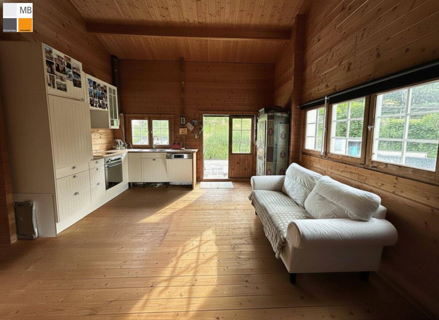 Gemütlicher offener Wohnbereich mit Holzböden, Holzverkleidung und einer weißen Einbauküche.
