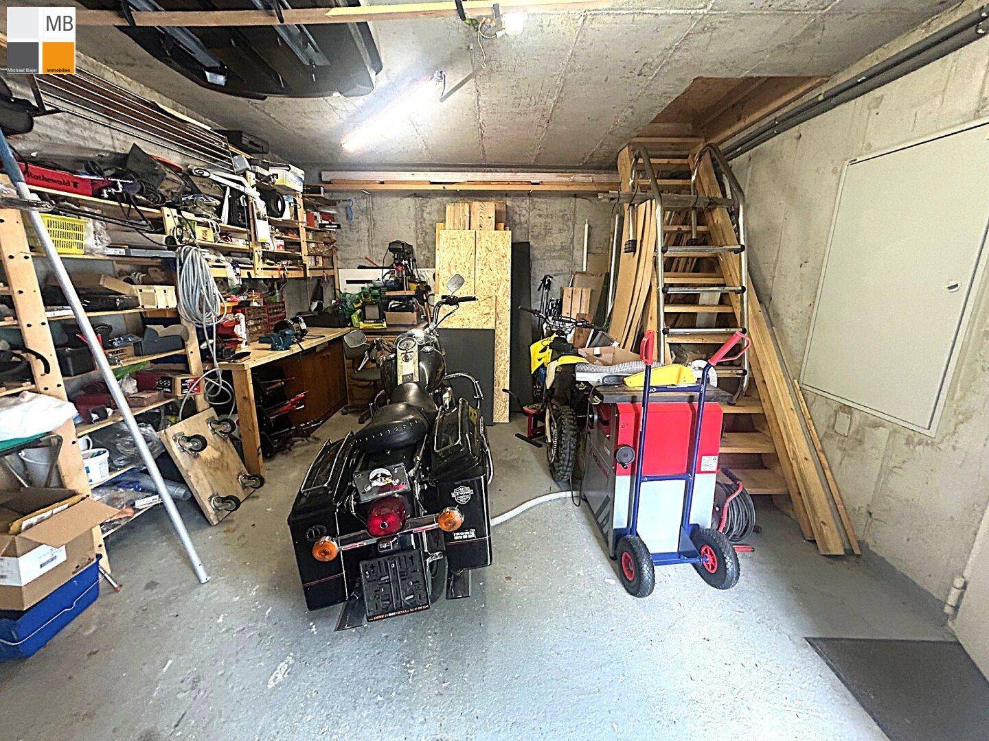 Geräumige Garage mit Betonboden, Regalen und Stauraum, inklusive Treppe zum oberen Bereich.