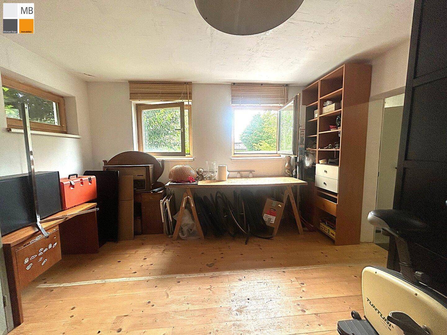 Vielseitiger Raum mit Holzboden und Fenstern, derzeit als Büro und Hobbyraum genutzt.