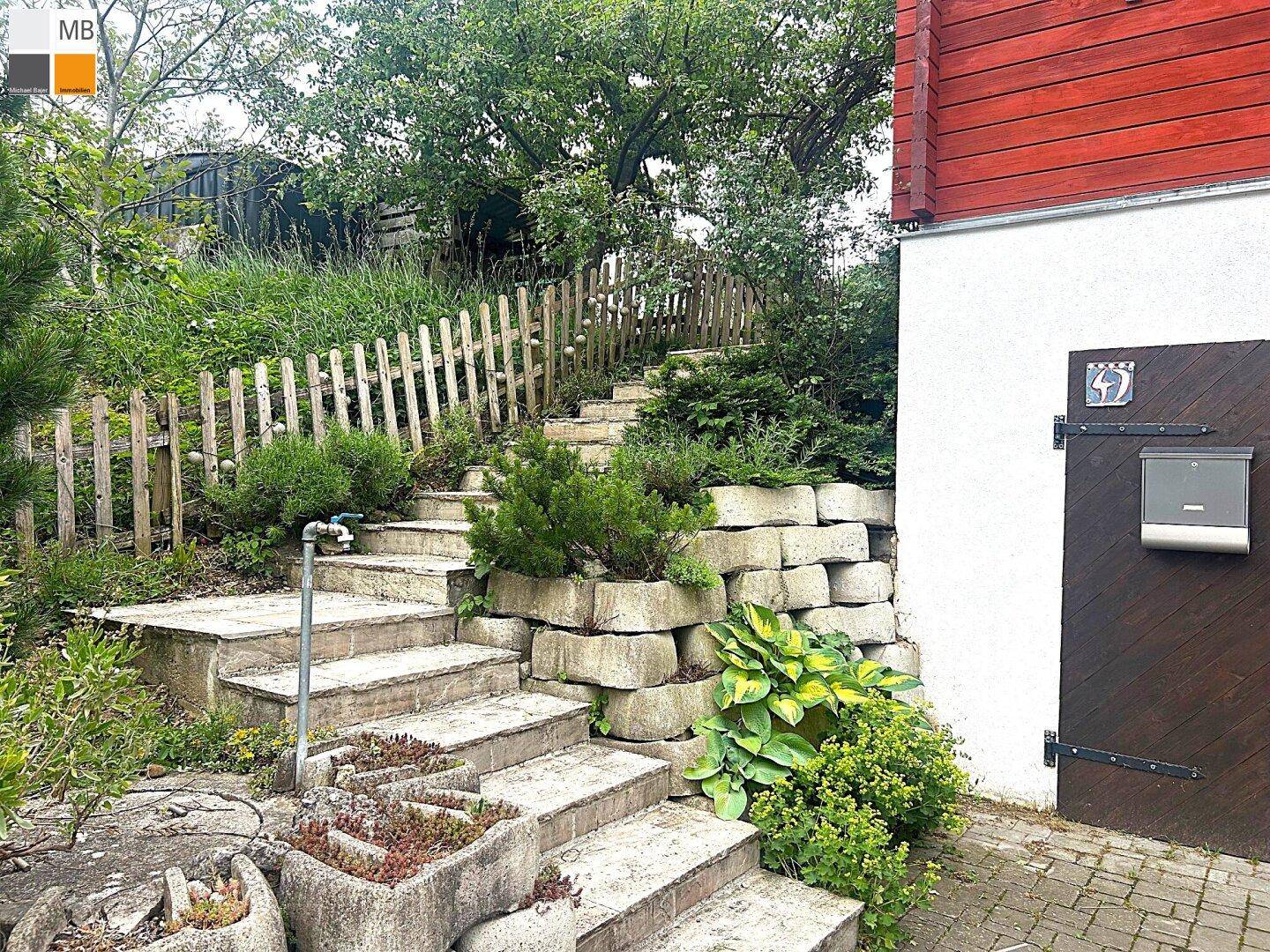 Steintreppe führt durch den Garten mit Blumenbeeten und einem Holzzaun den Hang hinauf.