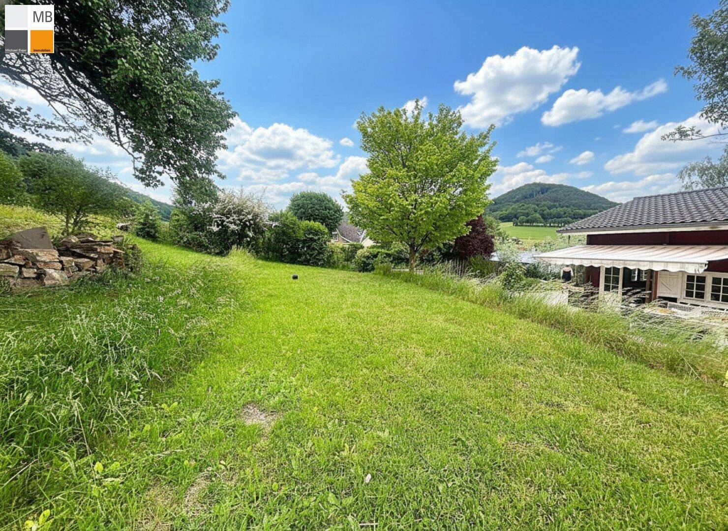 Großer grüner Rasenbereich mit Blick auf das Haus und die umliegende hügelige Landschaft.
