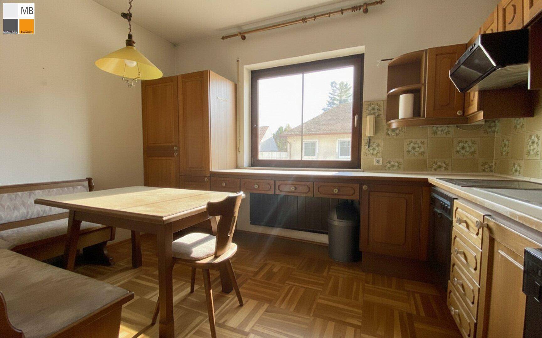 Traditionelle Küche mit Holzeinbauten, Essbereich und großem Fenster mit viel Sonnenlicht.