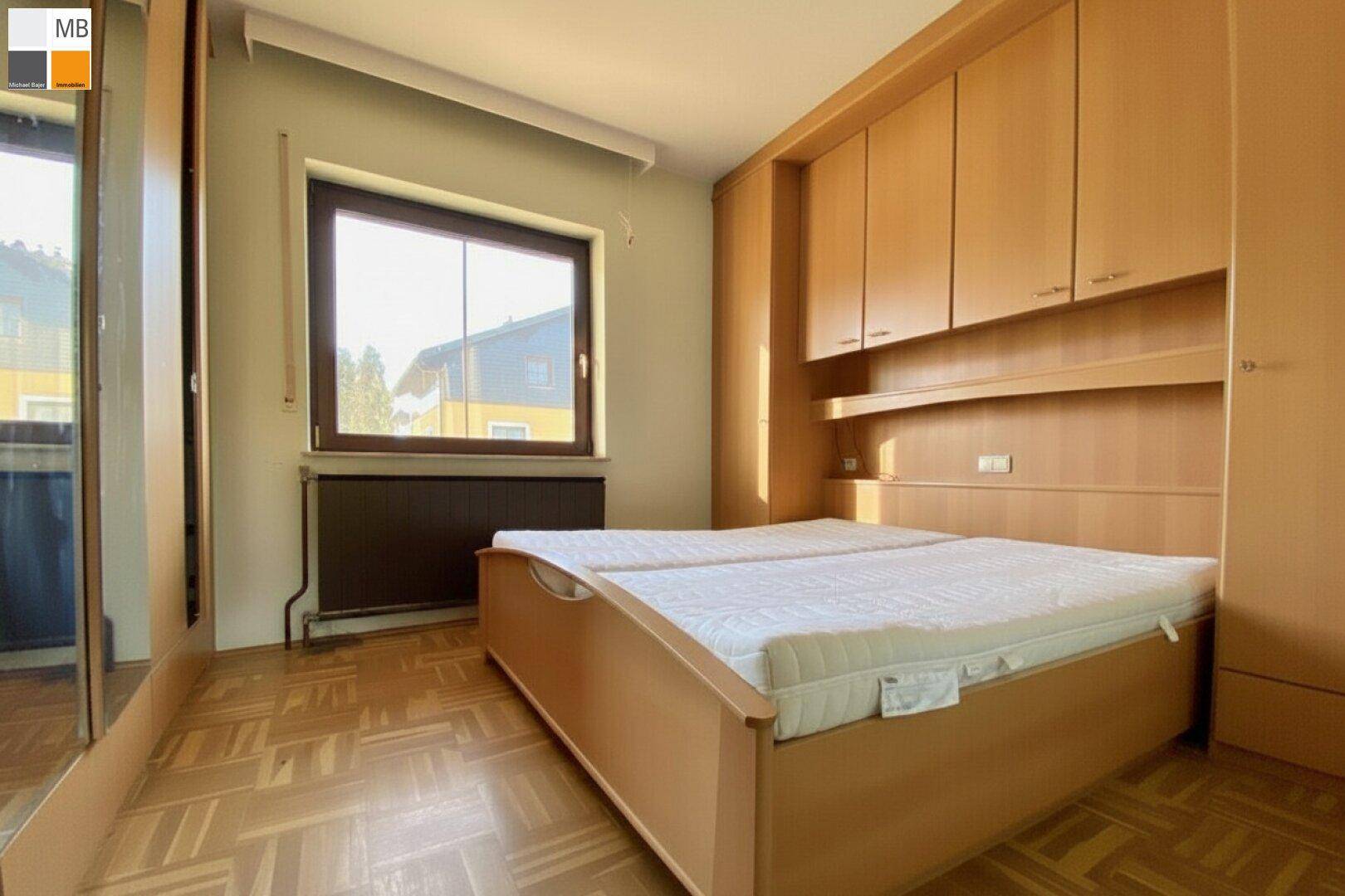 Schlafzimmer mit Einbauschränken, Parkettboden und großem Fenster für viel Helligkeit.
