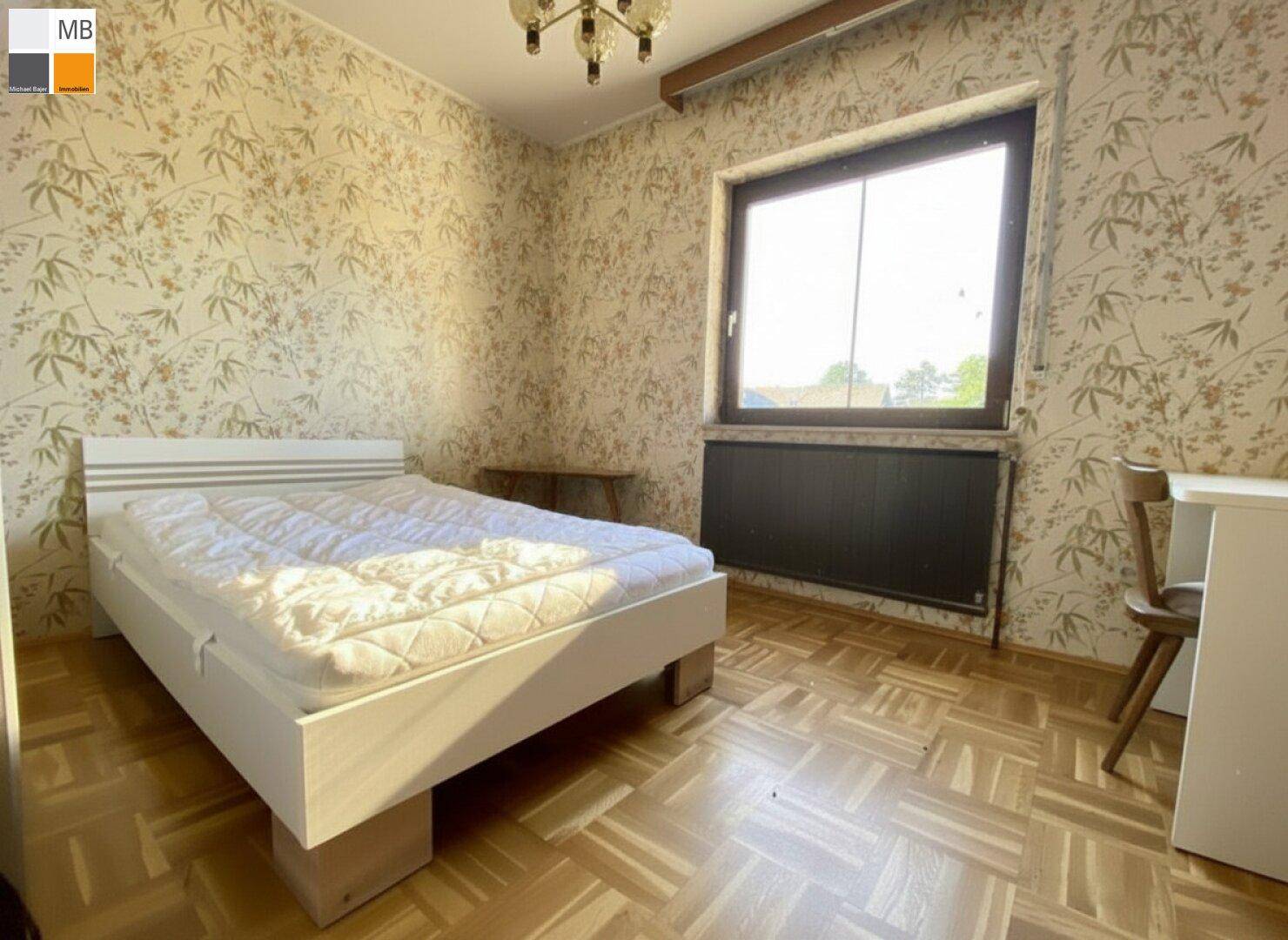 Helles Schlafzimmer mit Parkettboden, gemusterter Tapete und großem Fenster.