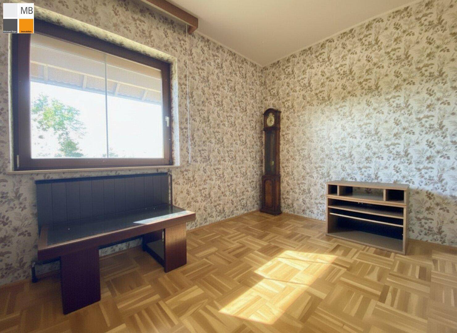 Vielseitig nutzbarer Raum mit Parkettboden, großem Fenster und traditioneller Standuhr.