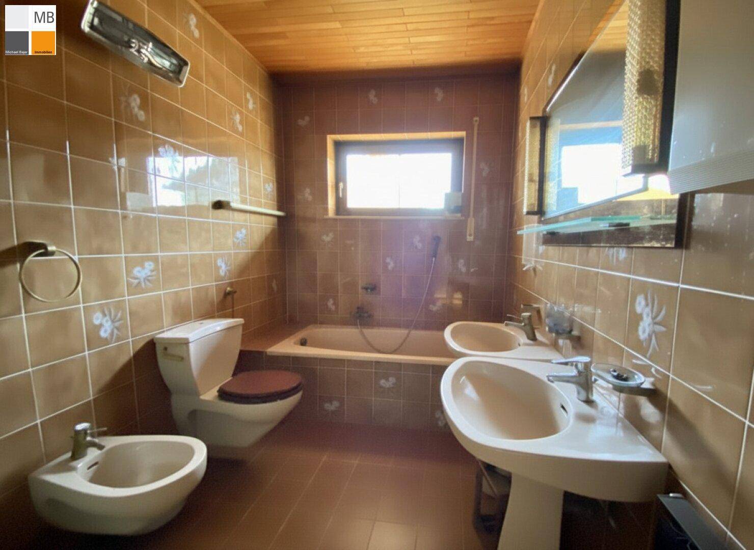 Badezimmer mit braunen Fliesen, Badewanne, Doppelwaschbecken und Bidet.