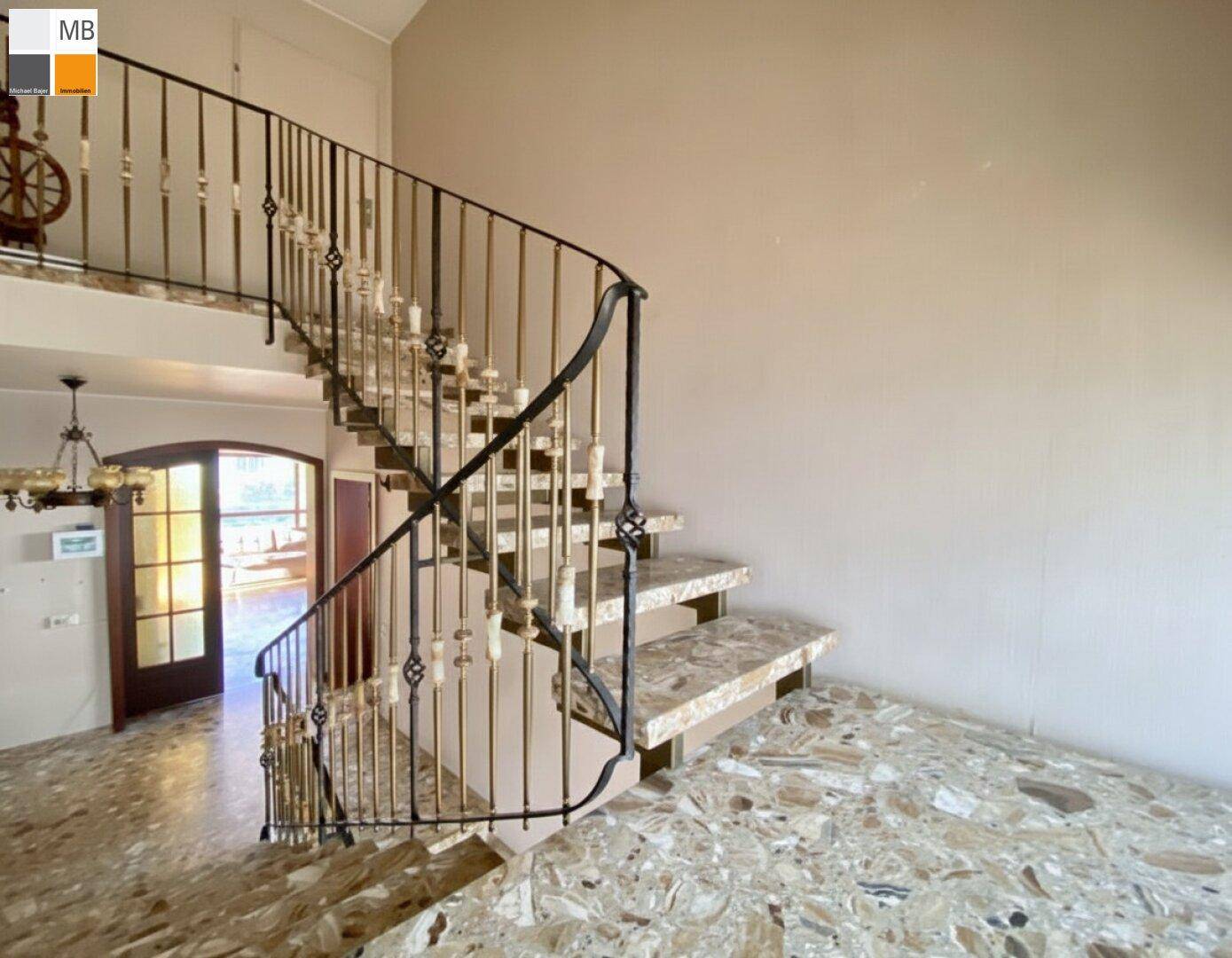 Elegante Treppe mit schmiedeeisernem Geländer und Marmorboden in einem hellen Flur.