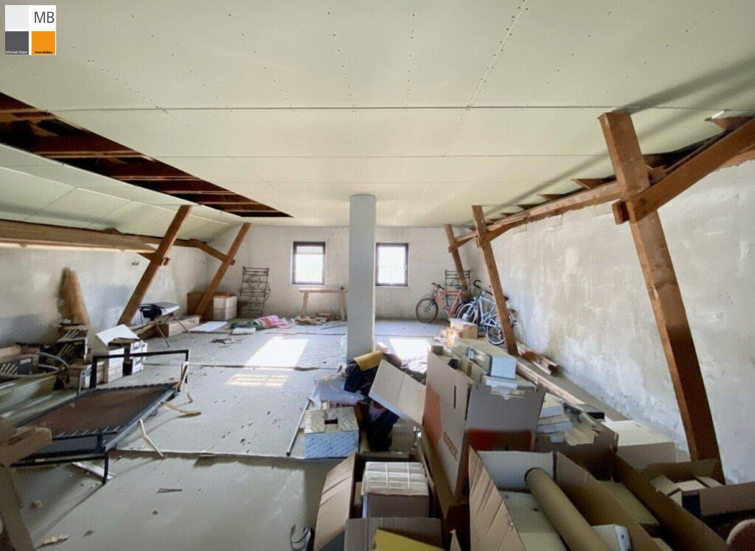 Ausbaufähiger Dachboden mit sichtbaren Holzbalken und Fenstern für Tageslicht.