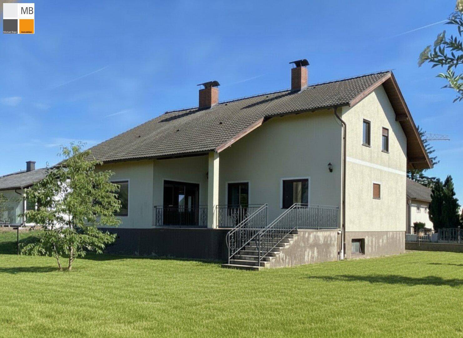 Rückansicht des Hauses mit überdachter Terrasse und Treppenzugang zum weitläufigen Garten.