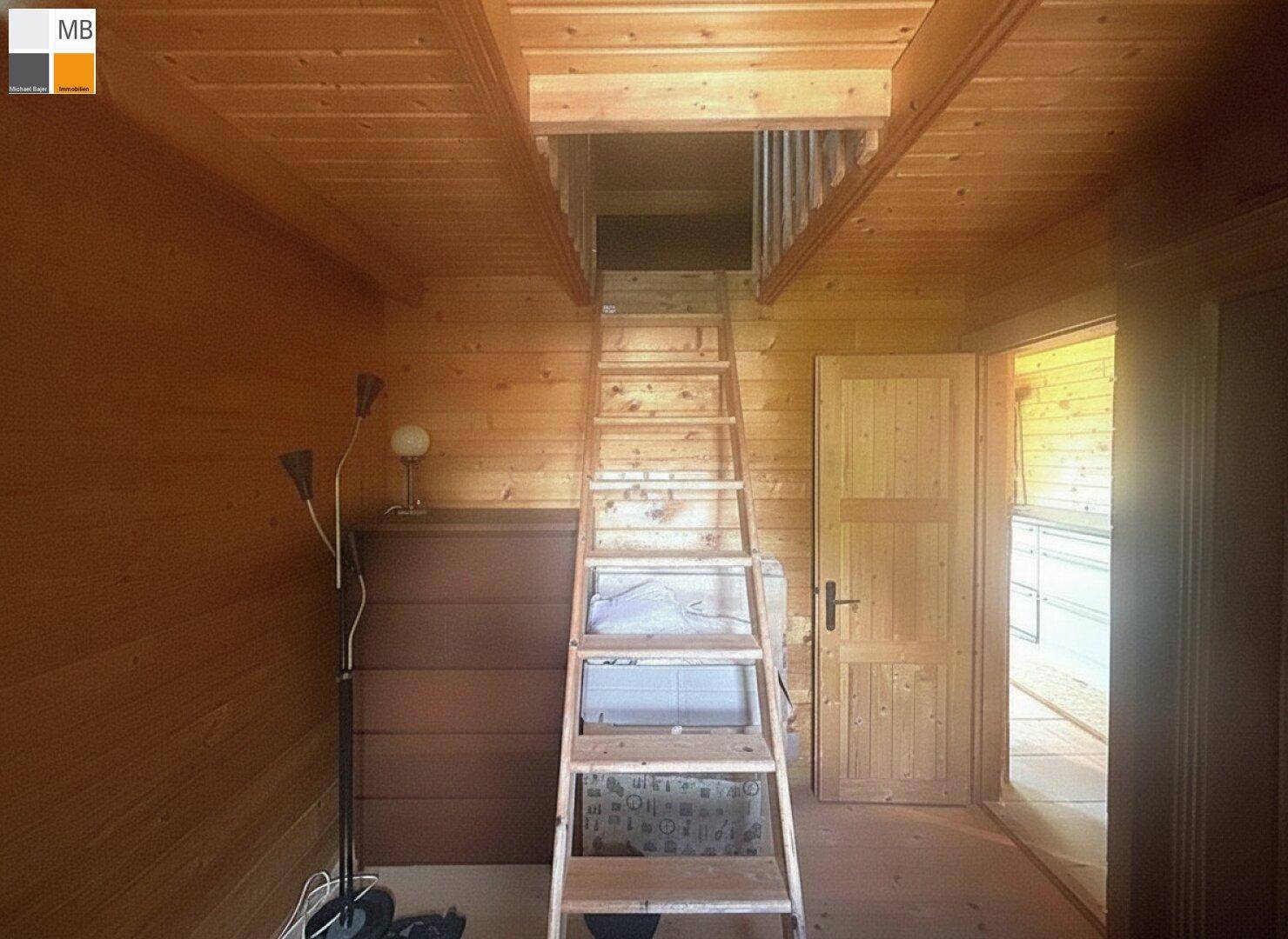 Rustikaler Innenraum mit Holzverkleidung und einer steilen Holzleiter, die zum Dachboden führt.