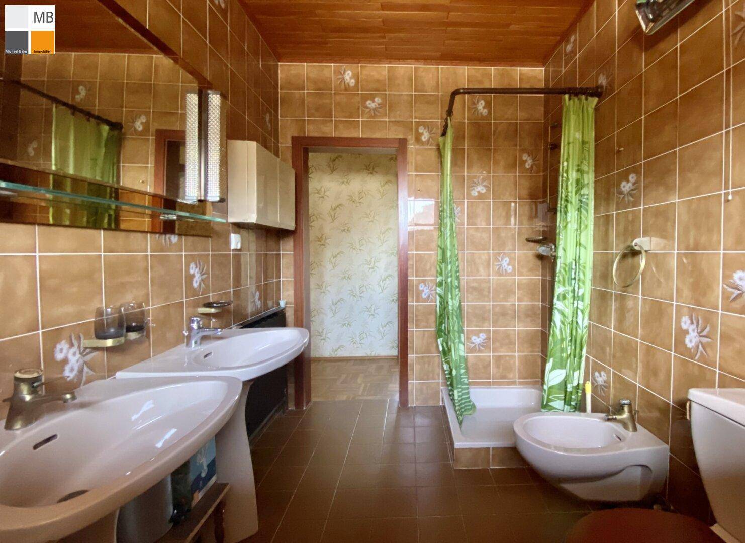 Badezimmer mit braunen Fliesen, Holzdecke, Doppelwaschbecken, Dusche und Bidet in einem Stil der 80er Jahre.