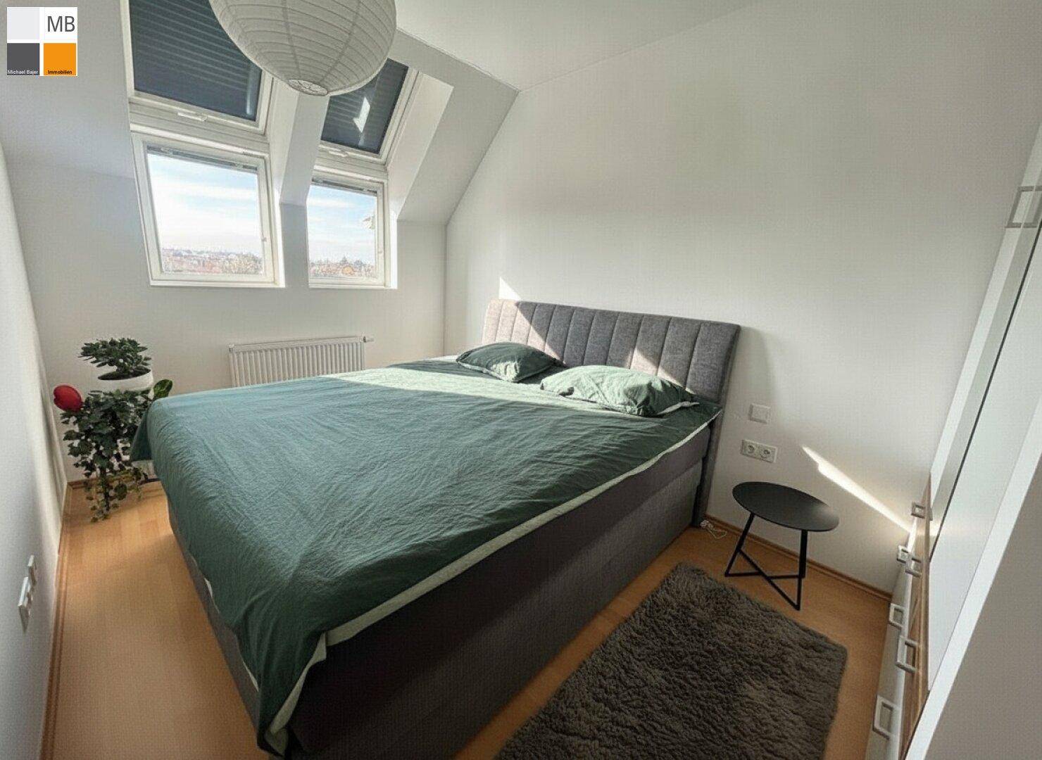 Helles Schlafzimmer mit Dachschrägen, zwei Dachfenstern und Doppelbett.