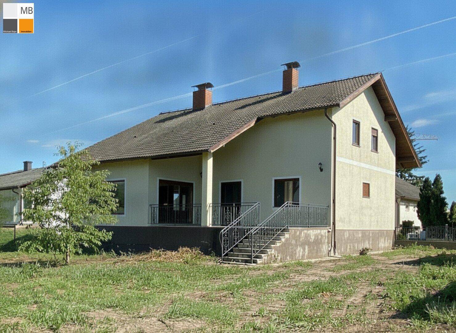 Freistehendes Haus mit heller Fassade, Ziegeldach und großem Grundstück unter blauem Himmel.