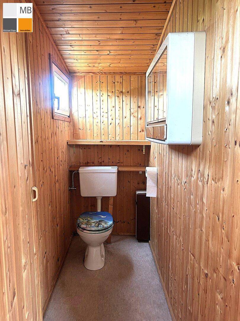 Schmale Toilette mit Holzvertäfelung und kleinem Fenster für natürliche Belüftung.