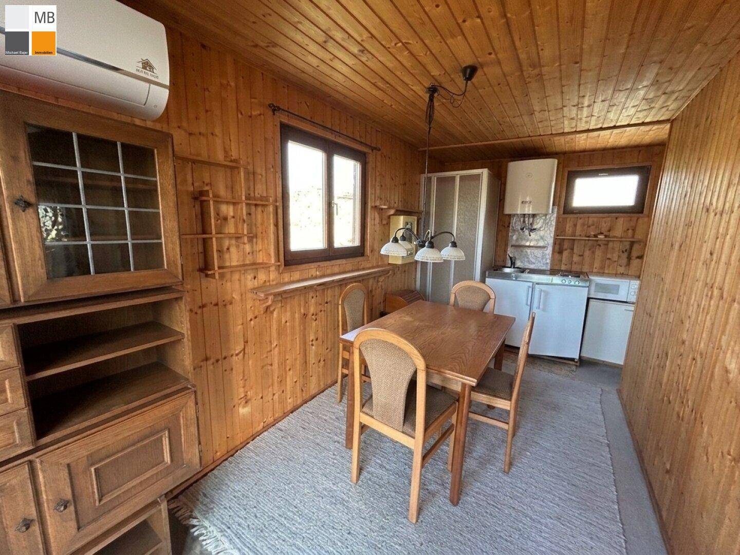 Gemütlicher Raum mit Holzvertäfelung, Esstisch und kleiner Küchenzeile im Landhausstil.