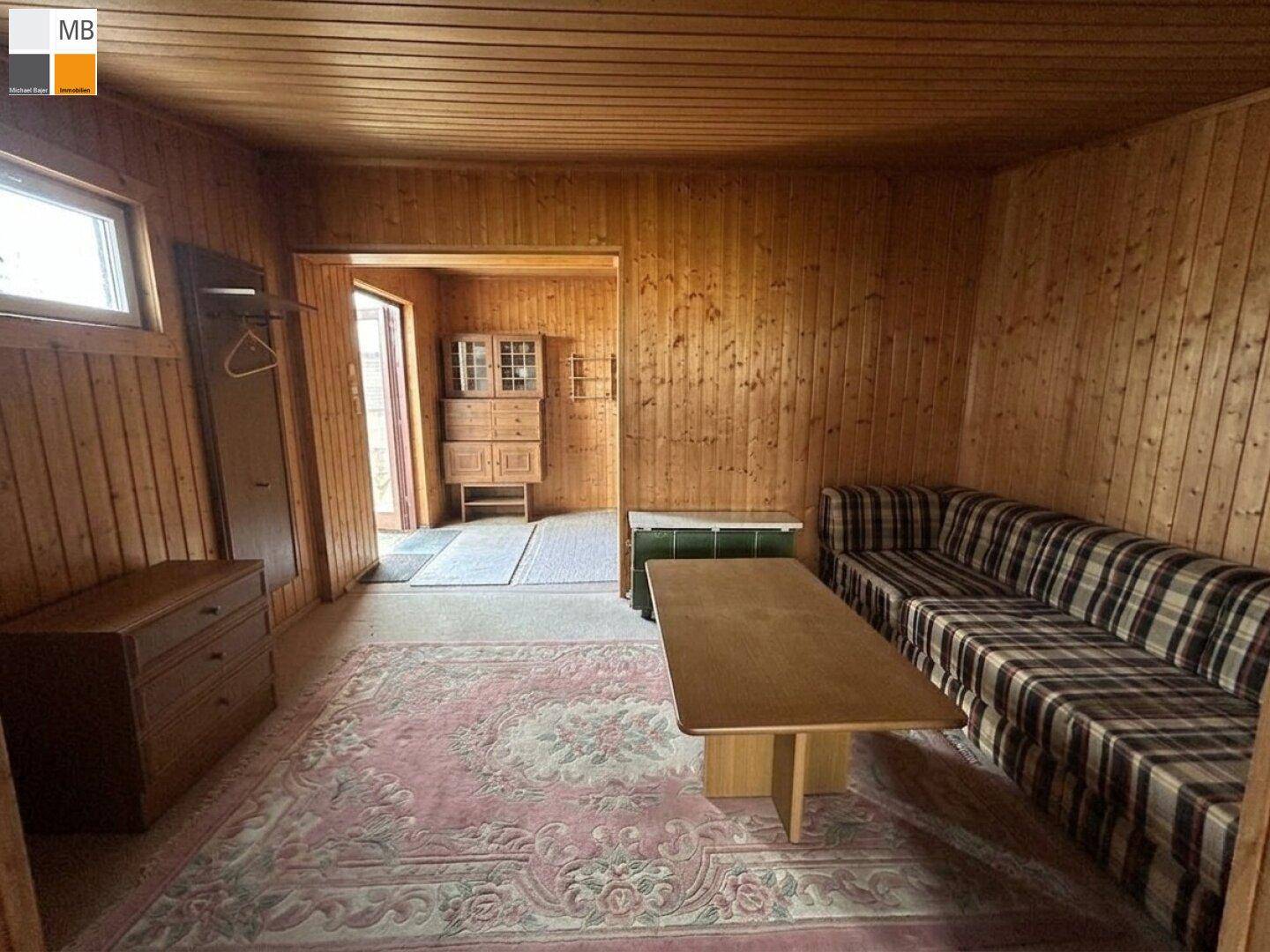 Gemütliches Wohnzimmer mit Holzvertäfelung, kariertem Sofa und Blick in den Nebenraum.