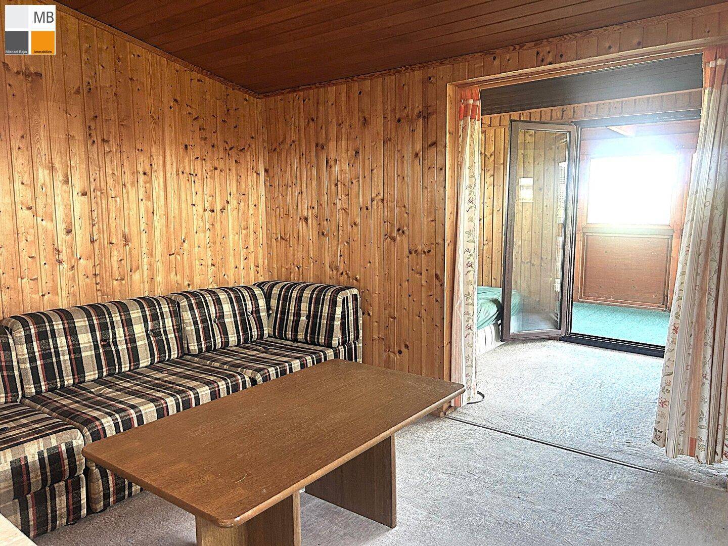 Wohnzimmer mit Holzvertäfelung und direktem Zugang zu einem hellen, verglasten Anbau.