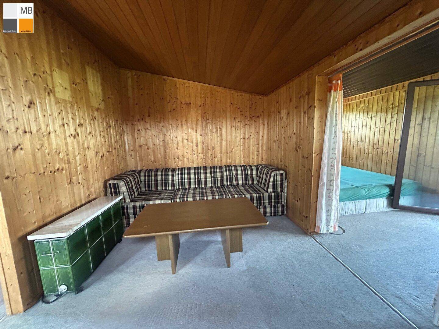 Wohnzimmer mit Holzvertäfelung, Sofa und einem traditionellen grünen Kachelofen.