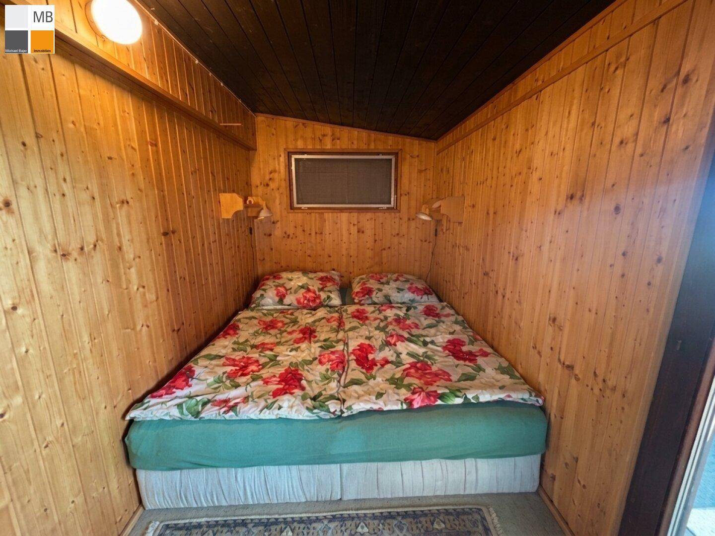 Kleines Schlafzimmer mit Holzvertäfelung, Doppelbett und floral gemusterter Bettwäsche.