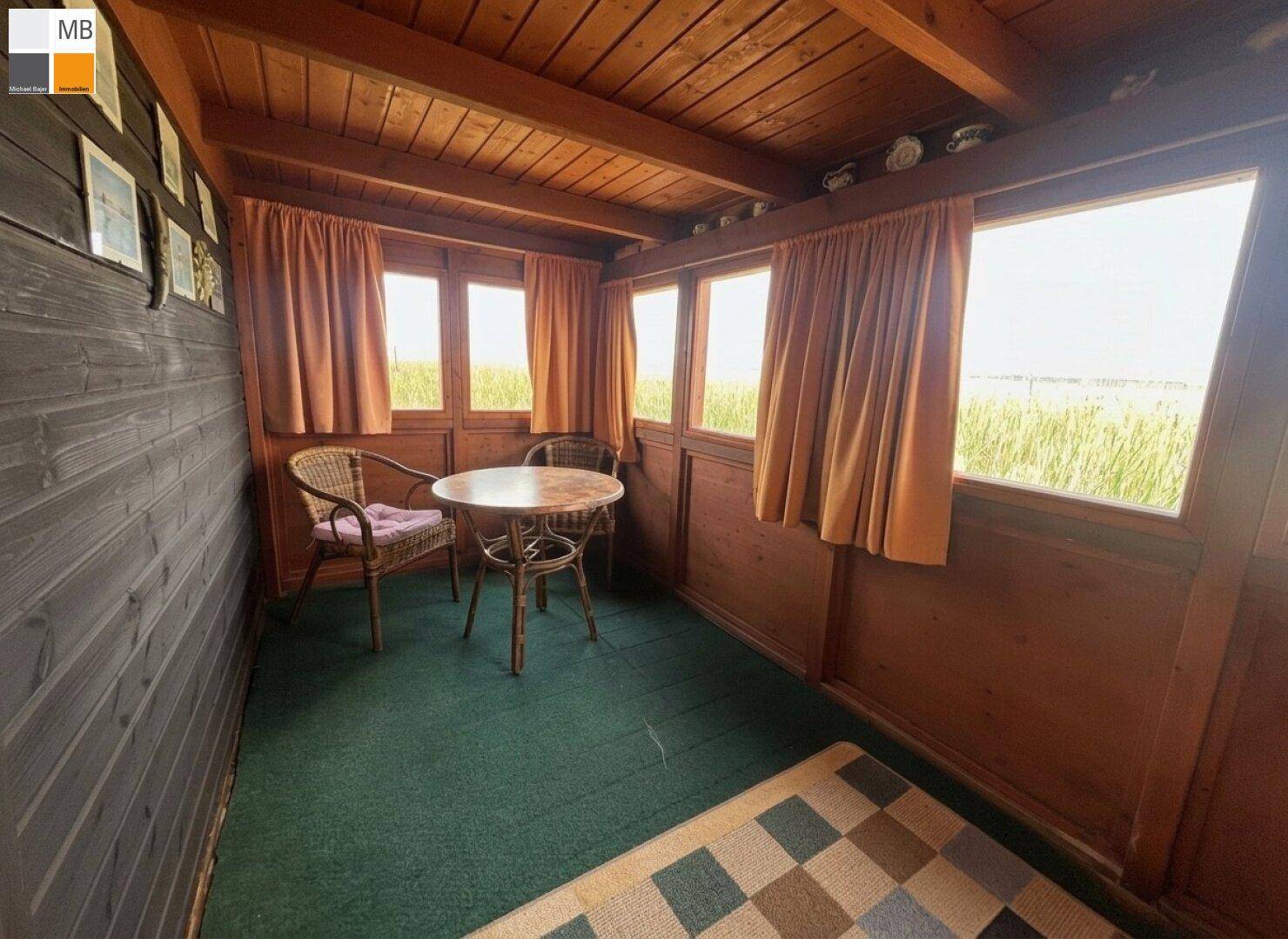 Verglaste Veranda mit Sitzgelegenheiten und weitem Blick auf die umliegende Naturlandschaft.