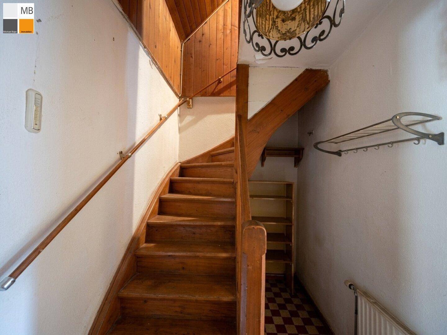 Holztreppe mit Geländer und kariertem Fliesenboden, die in die oberen Stockwerke führt.