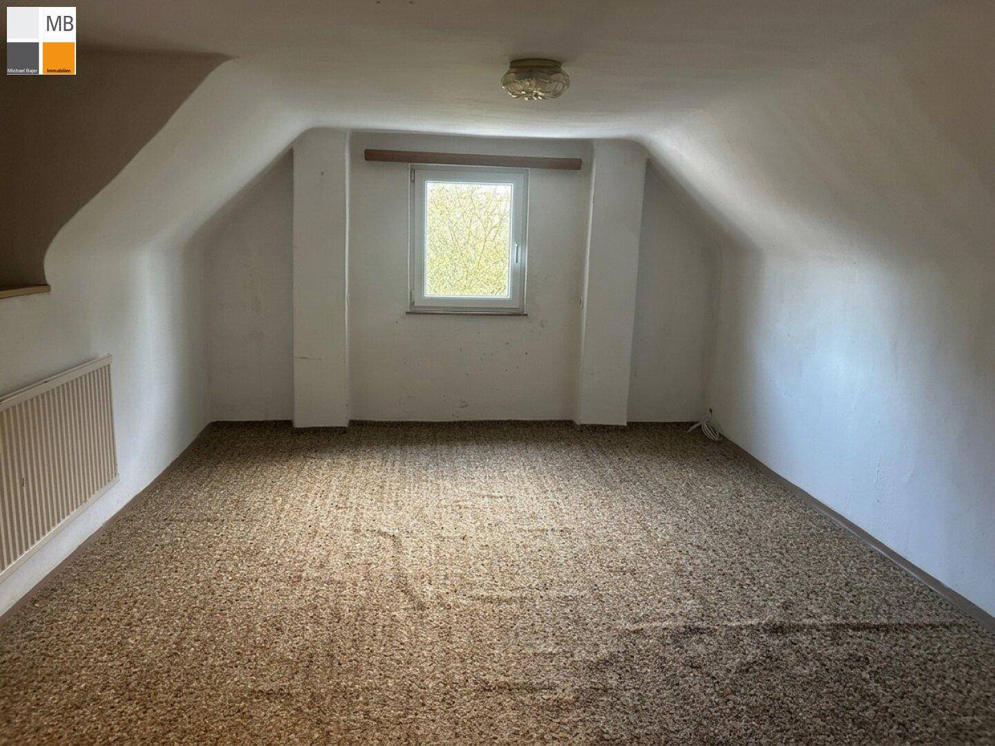 Dachgeschossraum mit Teppichboden, schrägen Wänden und einem kleinen Fenster.