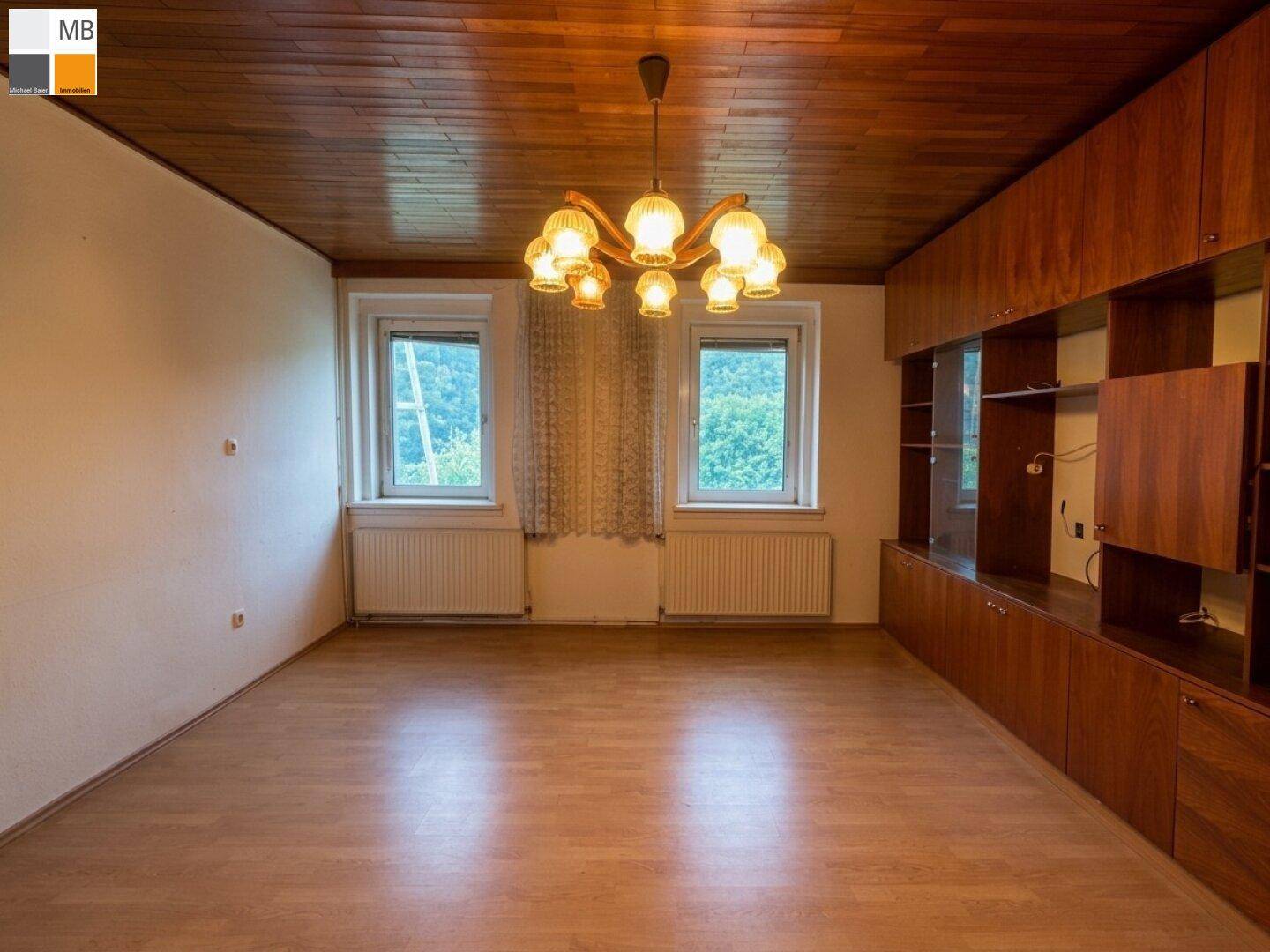 Geräumiges Wohnzimmer mit Holzdecke, Laminatboden und Einbauschränken entlang einer Wand.