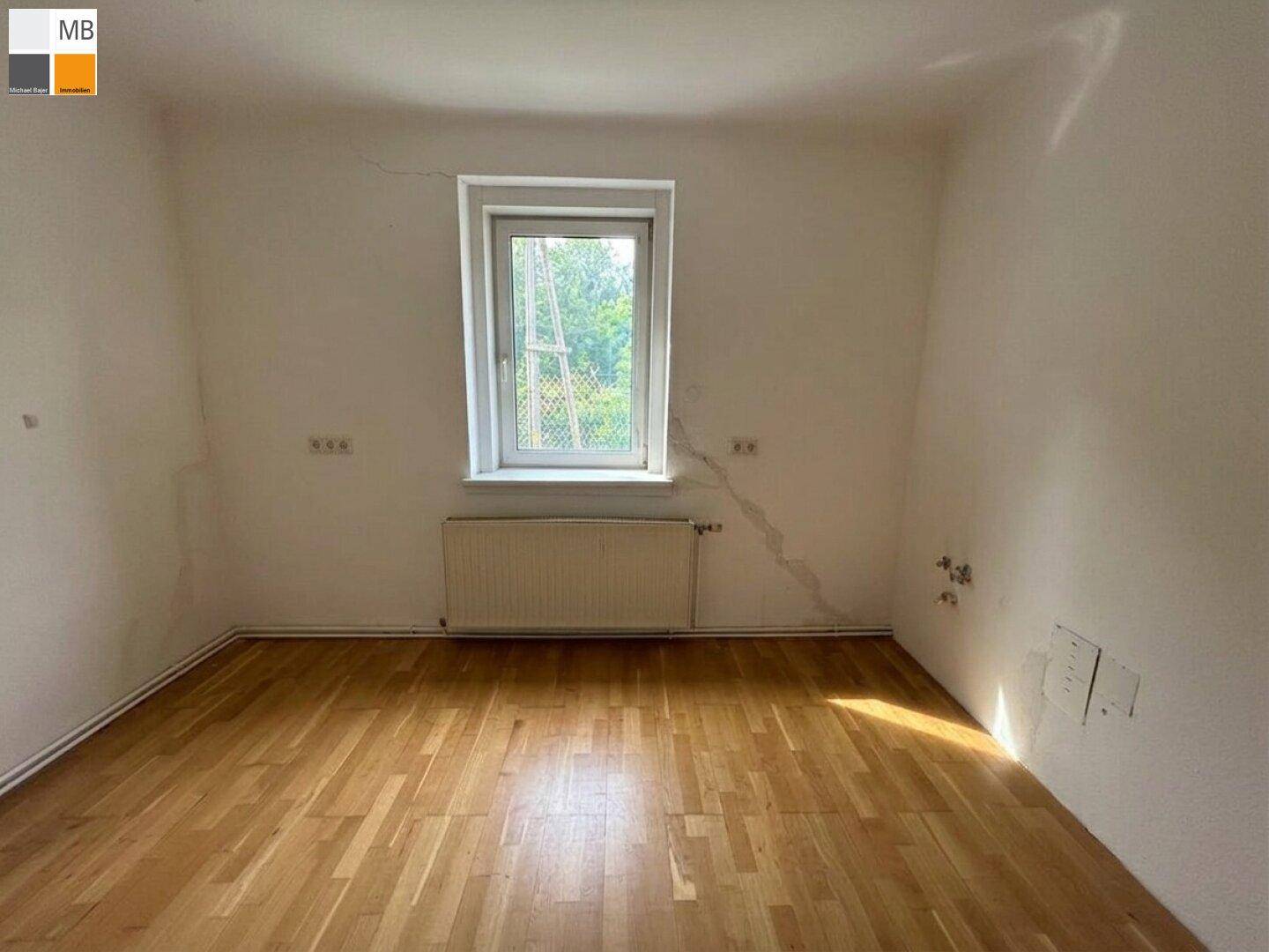 Helles Schlafzimmer mit Parkettboden und einem Fenster, das viel Tageslicht hereinlässt.
