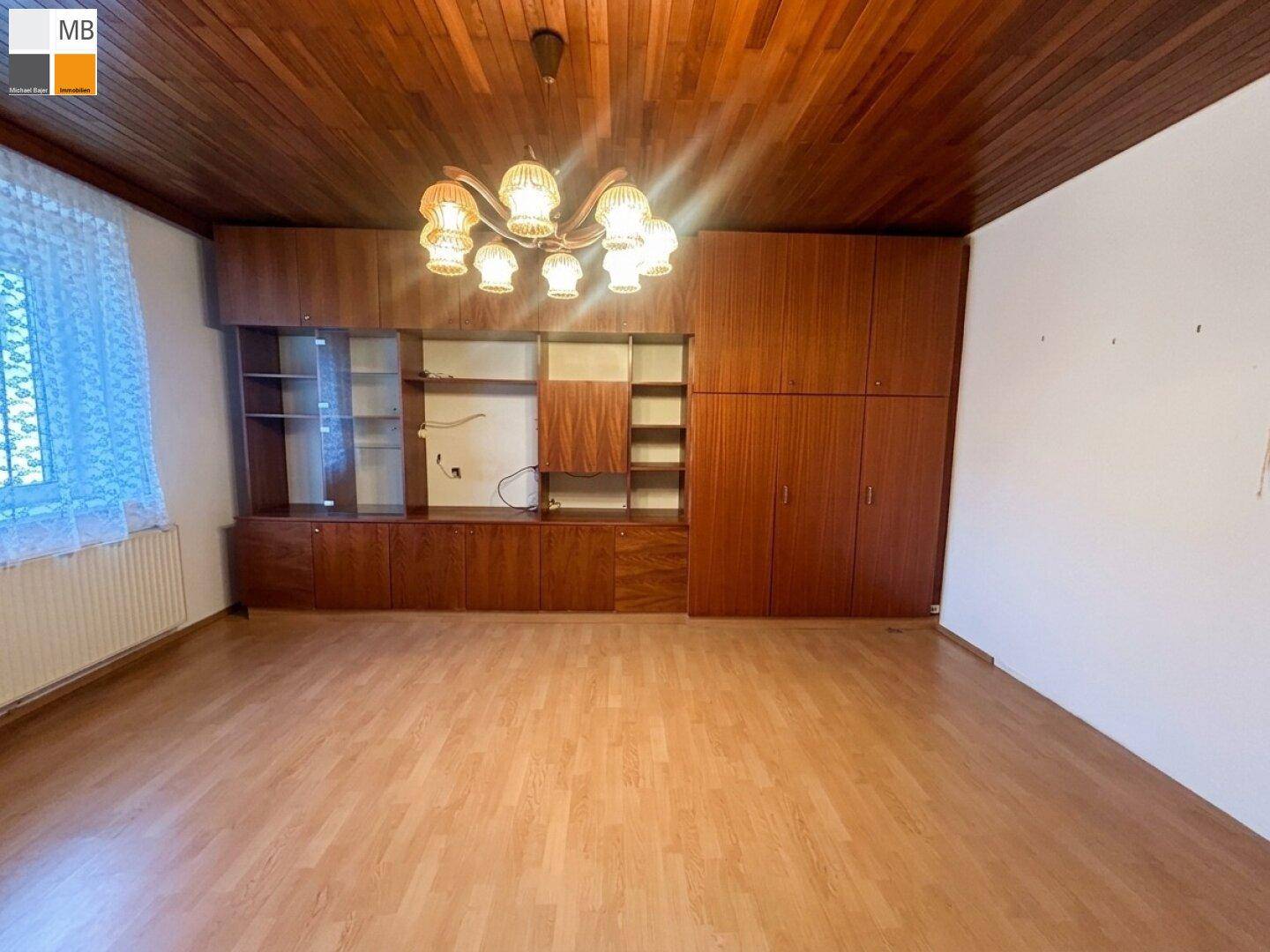 Wohnzimmer mit dunkler Holzdecke, Laminatboden und großer Schrankwand im klassischen Stil.