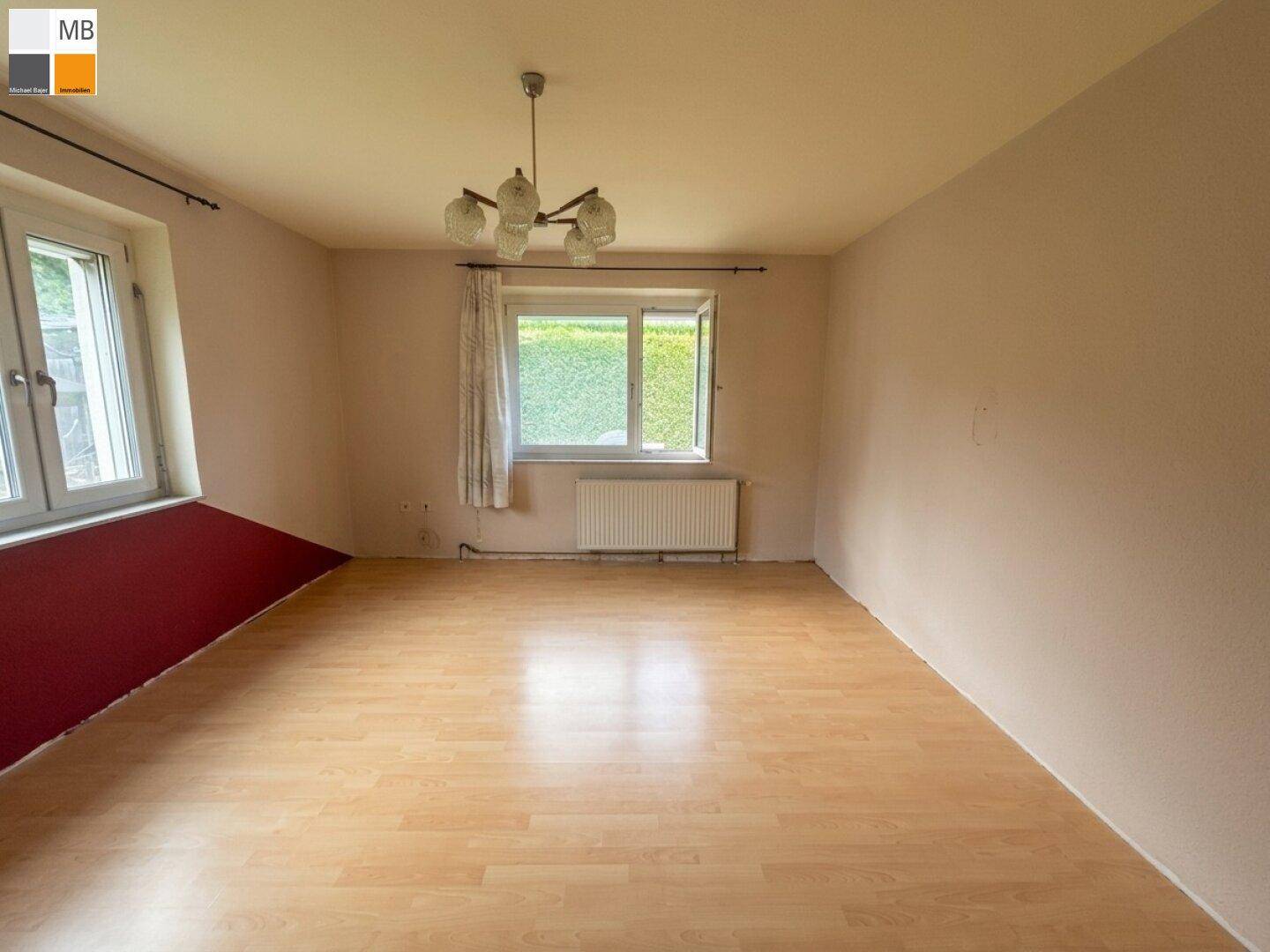 Helles Schlafzimmer mit Laminatboden, schlichter Einrichtung und Fenster zum Garten.