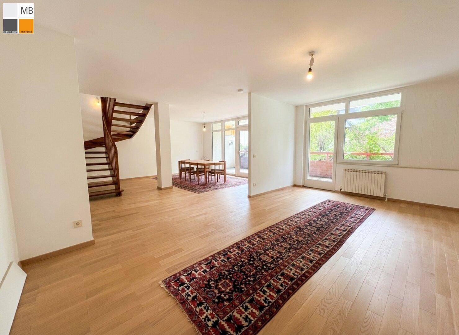 Geräumiges Wohn-Esszimmer mit hellem Parkettboden, Holztreppe und großen Fenstern.